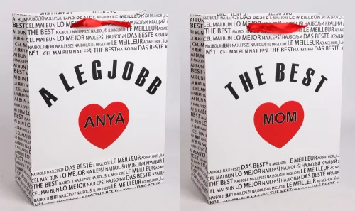 PAPÍRTASAK MATT, SZALAG FÜLLEL, FEHÉR ALAPON FEKETE NEMZETKÖZI ÍRÁSSAL A HÁTTÉRBEN, A LEGJOBB ANYA/ THE BEST MOM FELIRATTAL, PIROS SZÍVVEL